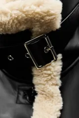 Cazadora de cuero sintético negro con interior de borreguillo color crema. Tiene cuello solapa, mangas largas, bolsillos delanteros y cierre con botones.