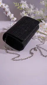 Sobre negro de textura elegante, con cadena para llevar al hombro, ideal para ocasiones especiales.