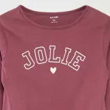 Conjunto de pijama de dos piezas color rosa, compuesto por una camiseta de manga larga con estampado frontal de la palabra "Jolie" y un pantalón largo.