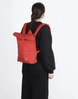 Mochila acolchada color ladrillo con cierre superior enrollable, correas ajustables y logo estampado en blanco.