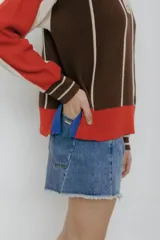 Buzo tipo polo de punto con rayas verticales en tonos beige, marrón y rosa. Tiene cuello polo marrón, cierre parcial con botones amarillos y terminaciones acanaladas en puños y ruedo.