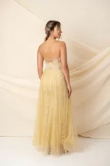 Vestido largo de tul bordado color dorado, con corsé transparente, breteles finos bordados, cintura con alforzas y bordado en hilo de seda, y falda de tul bordado con sobrefalda de tul plisado.