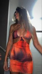 Vestido corto ajustado al cuerpo, con estampado abstracto en tonos naranja y marrón. Presenta escote asimétrico con abertura en el pecho y espalda descubierta.