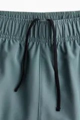 Short deportivo a media pierna en tejido funcional DryMove™ color verde azulado, con cintura elástica y cordón de ajuste oculto. Incluye bolsillos laterales y suspensor interior de malla.