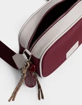 Bandolera de cuerina azul marino y beige con correa regulable azul y charm lateral decorativo. Tiene cierre superior y tag frontal con logo "The Brunch Club".