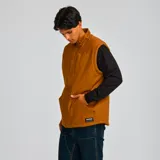 Chaleco marrón con cierre frontal, cuello alto y forro de poliéster tipo sherpa. Cuenta con un bolsillo con cierre en el pecho, dos bolsillos tipo canguro con remaches y dos bolsillos interiores.