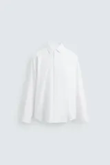 Camisa blanca de algodón, corte regular fit, cuello italiano, manga larga con puños abotonados y cierre frontal con botones.