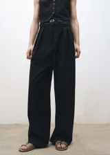 Pantalón negro de vestir, corte wide leg, con pinzas delanteras, trabillas y cinturón fino con hebilla metálica.