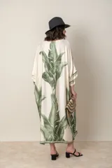 Vestido largo color natural con estampado de hojas de palmera en tonos verdes. Tiene corte amplio tipo túnica, cuello redondo, mangas tres cuartos, bolsillos laterales y ruedo con ribete.