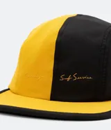 Gorra de cinco paneles bicolor, amarilla y negra, con visera plana y logo bordado en el panel frontal.