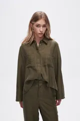 Camisa color natural de poliéster con cuello camisero, cierre con botones, dos bolsillos frontales y corte ancho.