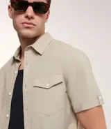 Camisa de hombre de manga corta en lino color blanco, con cuello clásico, botonadura frontal y bolsillo de parche en el pecho. Corte recto.