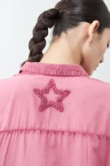 Camisa fucsia de manga larga con cuello camisero y cierre frontal con botones. Presenta apliques de estrellas bordadas en el frente y en el cuello.