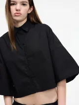 Camisa blanca cropped con botones en la parte delantera y mangas 3/4 con botones. Tiene pinza en la espalda.