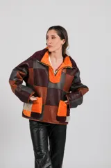Buzo tipo anorak de cuero genuino, reversible, con diseño de parches en tonos marrones, naranjas y grises. Presenta cuello con solapas y cierre parcial frontal. El forro interior es de pelo sintético en tonos naranja y marrón oscuro.