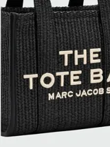 Bolso tote pequeño Marc Jacobs, tejido en color negro, con manijas cortas y correa larga ajustable. Estampado frontal con el texto "THE TOTE BAG MARC JACOBS" en color blanco.