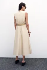 Vestido midi color beige, de popelín, con cuello redondo y sin mangas. Presenta cintura entallada con pinzas, cinturón y falda evasé.