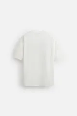 Camiseta blanca de corte relaxed fit, cuello redondo y manga corta. Presenta un bordado abstracto en color negro en el frente.