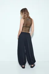 Pantalón blanco de tiro bajo, estilo baggy o aladín, con silueta amplia y fluida, cintura elastizada y puños ajustados en los tobillos.