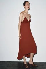 Vestido midi color ladrillo con tirantes finos, escote en pico y detalle de encaje en el busto. Tejido plisado y bajo asimétrico.
