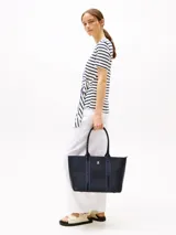 Bolso tote azul marino de poliuretano con cierre de cremallera, doble asa superior con inscripción de Tommy Hilfiger y logo TH dorado en el frente.