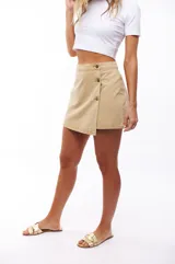 Falda short color beige con diseño cruzado y botones decorativos.