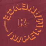 Remera bordó de manga corta con cuello redondo y estampado frontal con la letra K en color naranja.