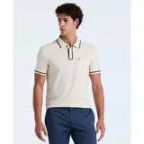 Polo color crema de algodón piqué, con cuello tipo camisa y cierre de botones. Tiene mangas cortas con ribete negro, bolsillo de parche en el pecho y logo bordado de pingüino.