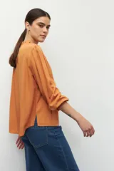 Camisa color naranja con cuello mao, escote en V, botones forrados y mangas largas con puños elásticos.