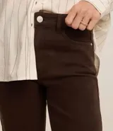 Pantalón slim de jeans color marrón, con cintura media, cierre tradicional con cremallera y botón, trabillas en la cintura, bolsillos delanteros y traseros con encaje.