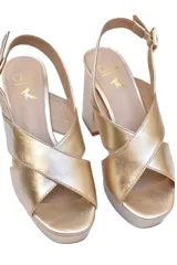 Sandalias de plataforma Cherie en cuero dorado metalizado. Diseño elegante con tiras cruzadas, pulsera ajustable al tobillo y tacón de bloque alto de aproximadamente 10 cm combinado con una plataforma delantera.
