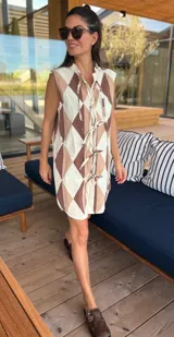 Vestido camisero corto con estampado de rombos en tonos beige, marrón y blanco. Tiene cuello camisero, cierre frontal con botones y corte holgado.