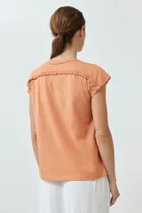 Remera color durazno con cuello en V y detalle de trenza en el escote.