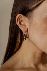 Aros colgantes dorados con forma de flor blanca.