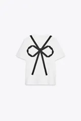 Camiseta blanca de corte recto, cuello redondo y mangas cortas. Presenta un lazo negro estampado en el frente.