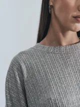 Sweater gris de tejido acanalado, manga larga y cuello redondo. Presenta un corte holgado con bajo redondeado y un pequeño parche negro con logo en la manga izquierda.