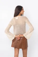 Top de tejido calado color marrón con mangas largas acampanadas y detalle de broches decorativos en el escote.