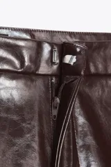 Shorts de tiro alto color marrón chocolate con efecto cuero. Presentan bolsillos laterales y falsos bolsillos de vivo en la espalda. Cierre frontal con cremallera y gancho metálico.