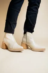 Botas cortas de cuero color crema, con puntera fina, paneles laterales con textura de piel de reptil, cierre lateral con cremallera y tacón geométrico de madera.