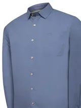 Camisa de manga larga color celeste, confeccionada en popelina de algodón orgánico. Tiene cuello clásico, cierre frontal con botones de madera, bolsillo en el pecho con logo bordado y mangas ajustables con botón.