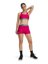 Top deportivo Under Armour HeatGear® Armour Mid Crossback, color fucsia, con logo blanco en el frente y banda elástica con la inscripción "Under Armour".