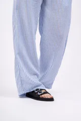 Pantalón largo de mujer, de corte amplio y tiro alto, con estampado a rayas verticales en tonos beige y blanco. Tiene cintura elástica con cordón ajustable.