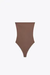 Body bandeau color marrón confeccionado en tejido elástico, con escote recto y hombros descubiertos. Cierre inferior con botones a presión.