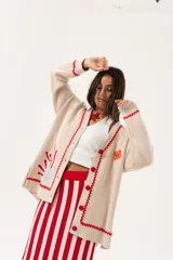 Saco oversize tejido con ilustraciones inspiradas en corales, peces, estrellas de mar y tortugas. Presenta galón picot en rojo en cartera y puños, y botones a tono.