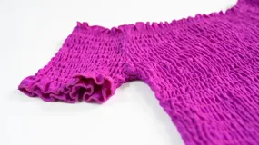 Top elastizado fucsia con mangas cortas con volados y hombros descubiertos.