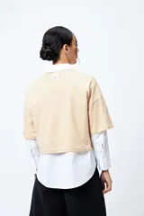 Remera blanca cropped de mangas cortas amplias con ojales metálicos a lo largo de las mangas.
