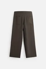 Pantalón marrón oscuro de corte amplio, con cintura ajustable con cordón, bolsillos plastrón delanteros y traseros, detalle de costuras frontales y cierre frontal con cremallera y gancho metálico oculto.