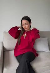 Canguro rojo de corte oversize con pinzas en las mangas, tajo a los lados y bolsillo tipo canguro. Tiene cuello con cordones ajustables.