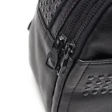 Mochila negra de cuero sintético con apliques de tachas redondas en el frente. Tiene asa de mano y tiras traseras regulables.