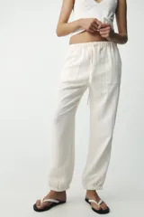 Pantalón jogger color gris claro, de tiro alto con cintura elástica ajustable con cordones, bolsillos delanteros y traseros con solapa, y puños elásticos en los tobillos.